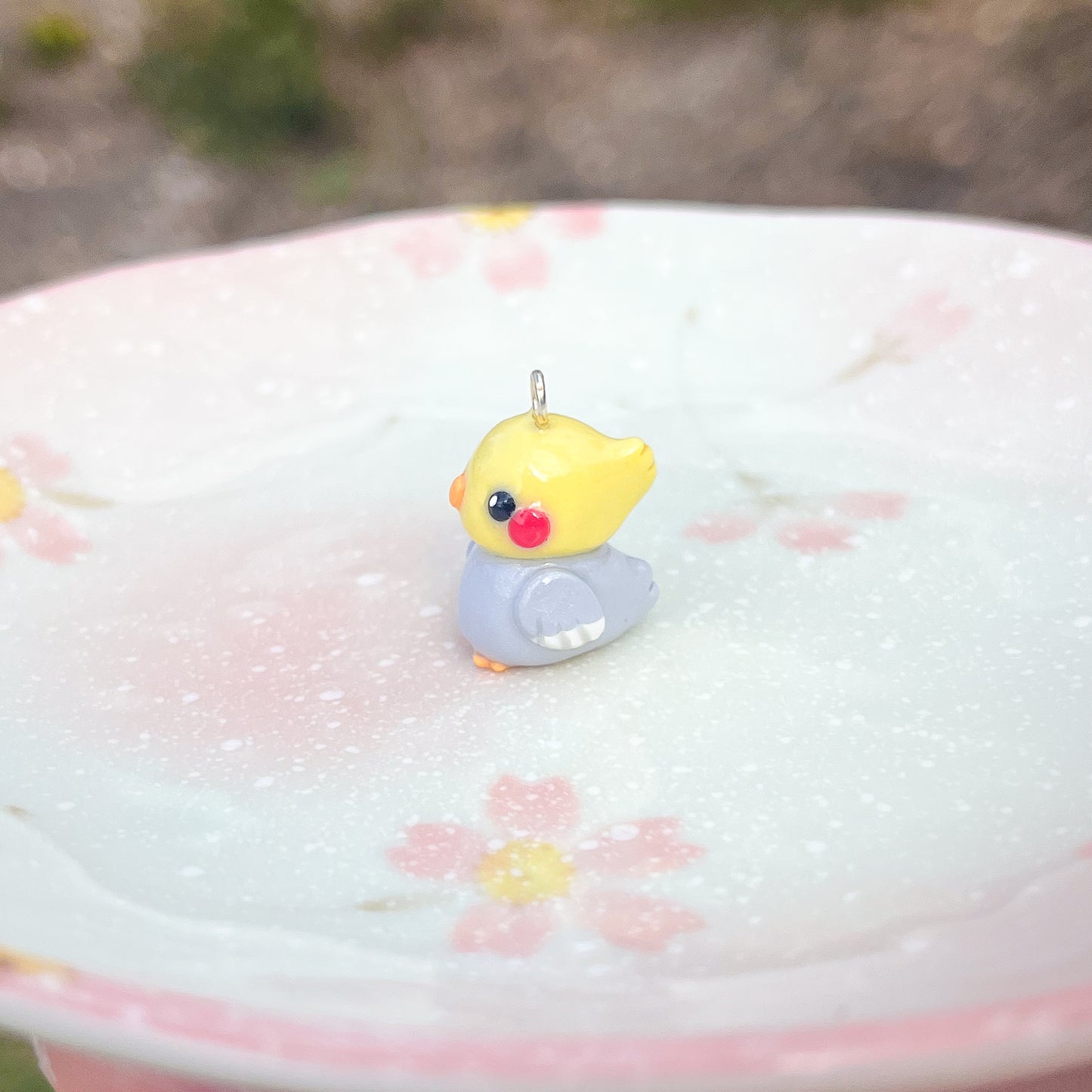 Handmade polymer clay cockatiel charms. This little bird has an orange beak/feet, and cute rosy-red cheeks.