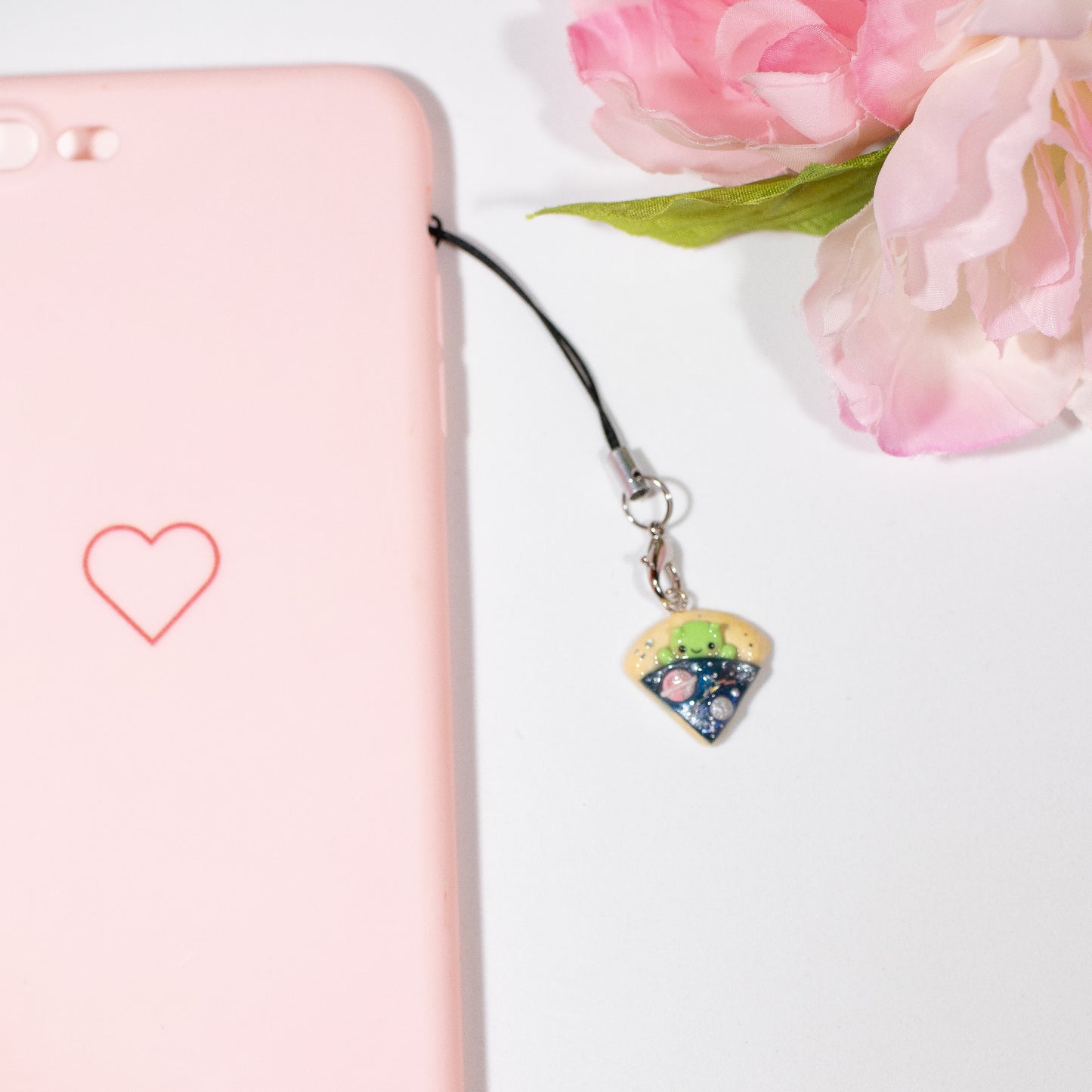 A simple alien pizza charm. This little charm has a tiny, green alien tucked inside a pizza. The pizza is galaxy-themed, with little planets, stars and glitter. This charm can be attached onto a cellphone, planner or purse!