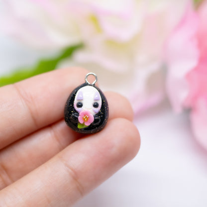 Handmade polymer clay no face charm inspired by the movie spirited away. The no face is holding a little pink cherry blossom flower token in it's hands.