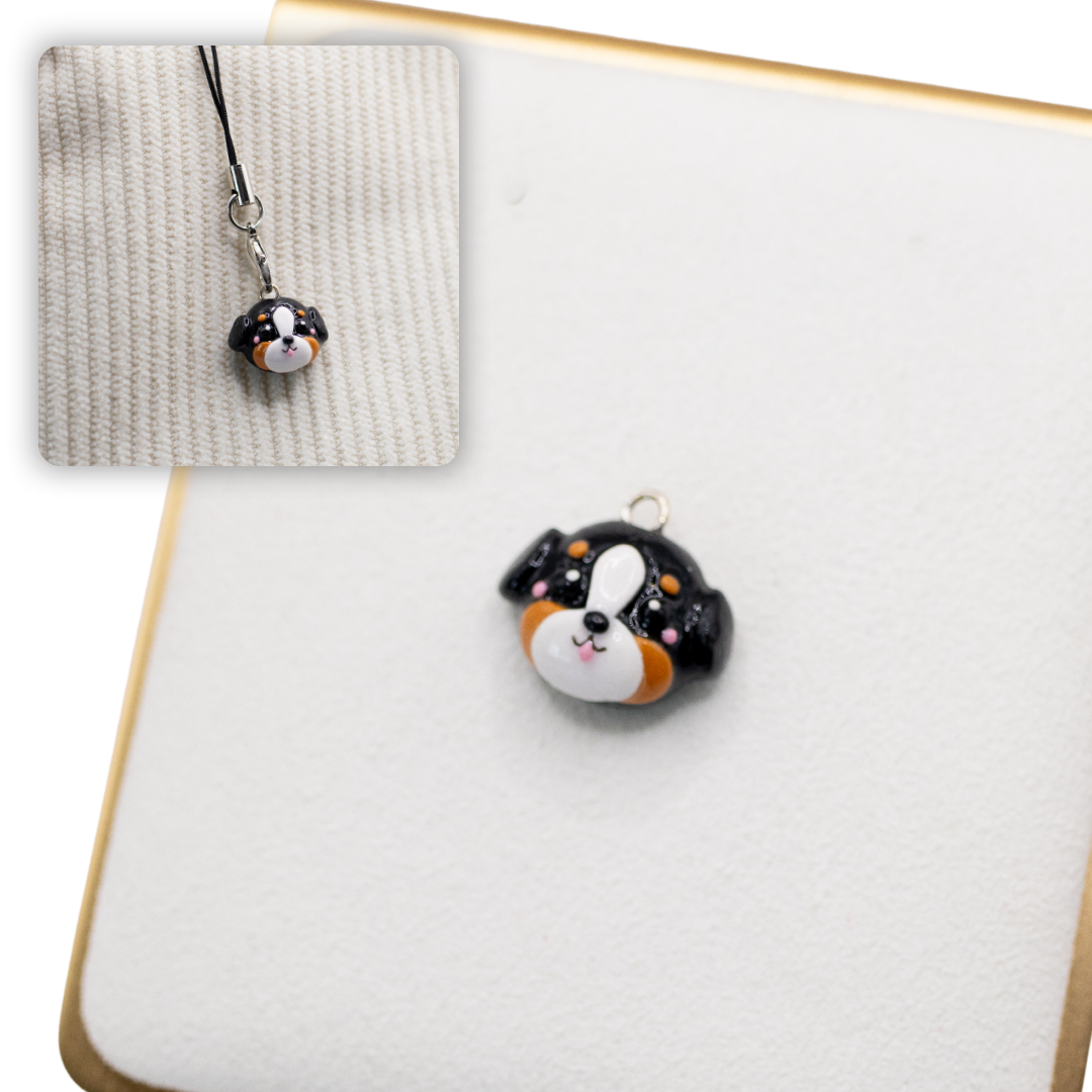A picture of a bernese mountain dog polymer clay dog charm against a white background, with a 2nd smaller photo of the same dog charm being hung with a phone strap against a textured background.