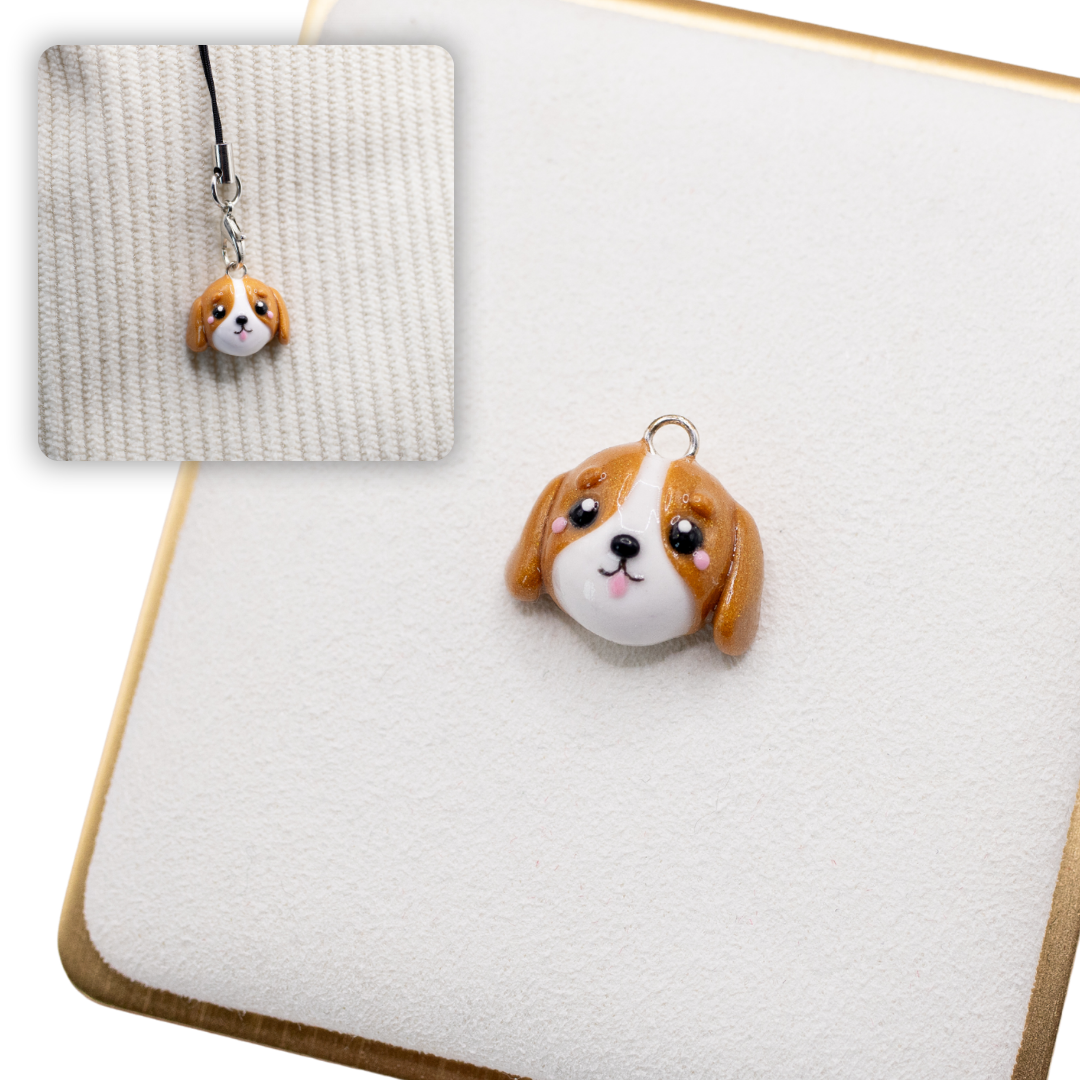 A picture of a cavalier king charles spaniel dog polymer clay charm on a white display with a gold border. There is a 2nd smaller photo of the same dog charm being hung with a phone strap against a textured background.