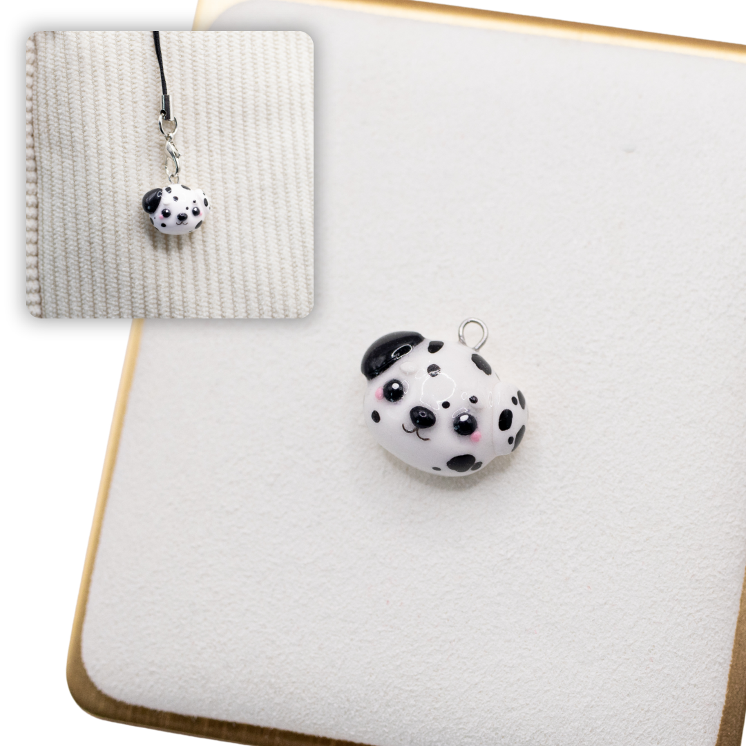 A picture of a dalmation polymer clay dog charm on a white display with a gold border. There is a 2nd smaller photo of the same dog charm being hung with a phone strap against a textured background.