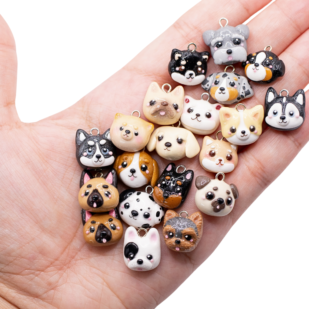 A hand holding a collection of 20 different handmade clay dog charms on a white background.