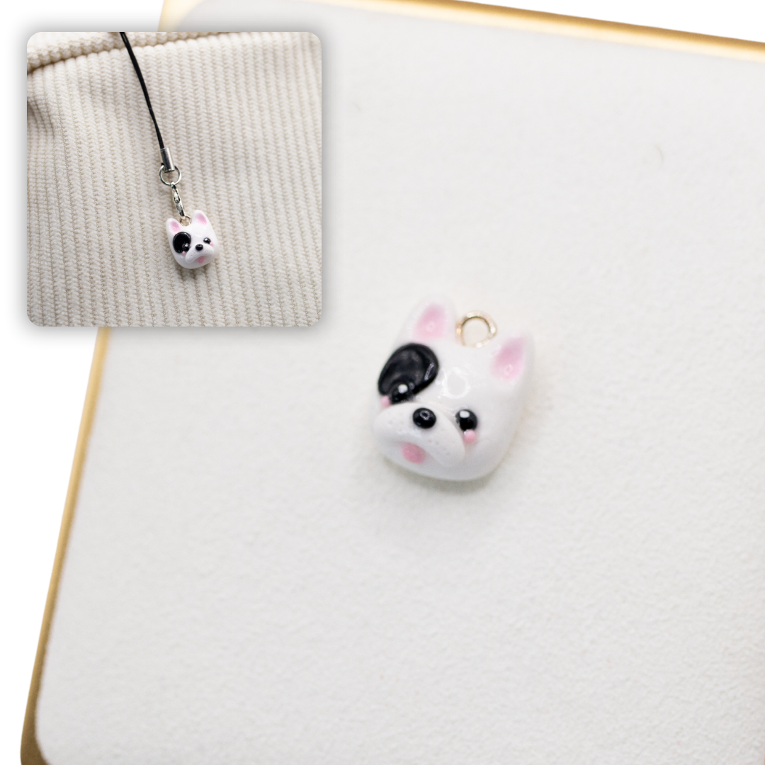 A picture of a white and black french bulldog polymer clay dog charm against a white background, with a 2nd smaller photo of the same dog charm being hung with a phone strap against a textured background.
