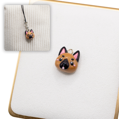 A picture of a german shepherd dog polymer clay dog charm on a white display with a gold border. There is a 2nd smaller photo of the same dog charm being hung with a phone strap against a textured background.
