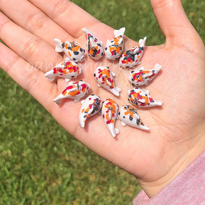 A handful of koi clay charms. These koi charms come in a variation of colors with red, orange, and black spots.