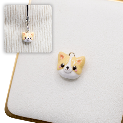 A picture of a pembroke welsh corgi polymer clay dog charm on a white display with a gold border. There is a 2nd smaller photo of the same dog charm being hung with a phone strap against a textured background.