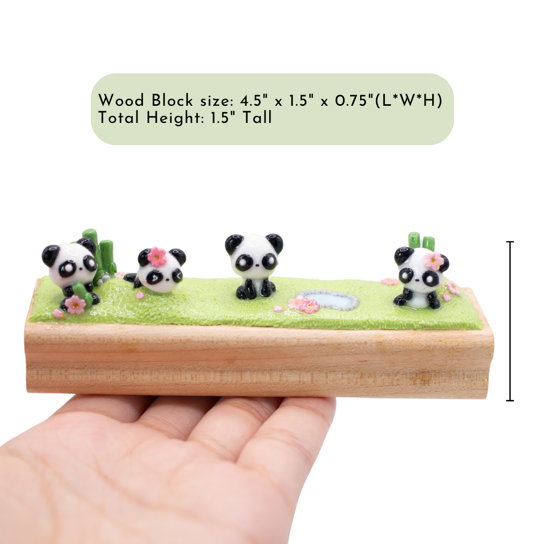 A small figurine of 4 pandas playing together on the grass on a wooden block with dimensions displayed. the dimensions are: 4.5" x 1.5" 1.5" (L*W*H)