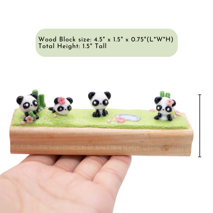 A small figurine of 4 pandas playing together on the grass on a wooden block with dimensions displayed. the dimensions are: 4.5" x 1.5" 1.5" (L*W*H)
