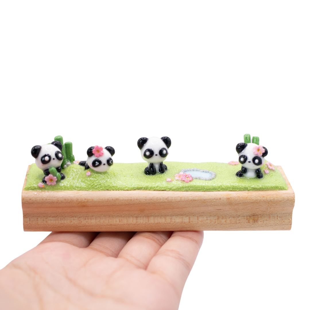 A small figurine of 4 pandas playing together on the grass on a wooden base.