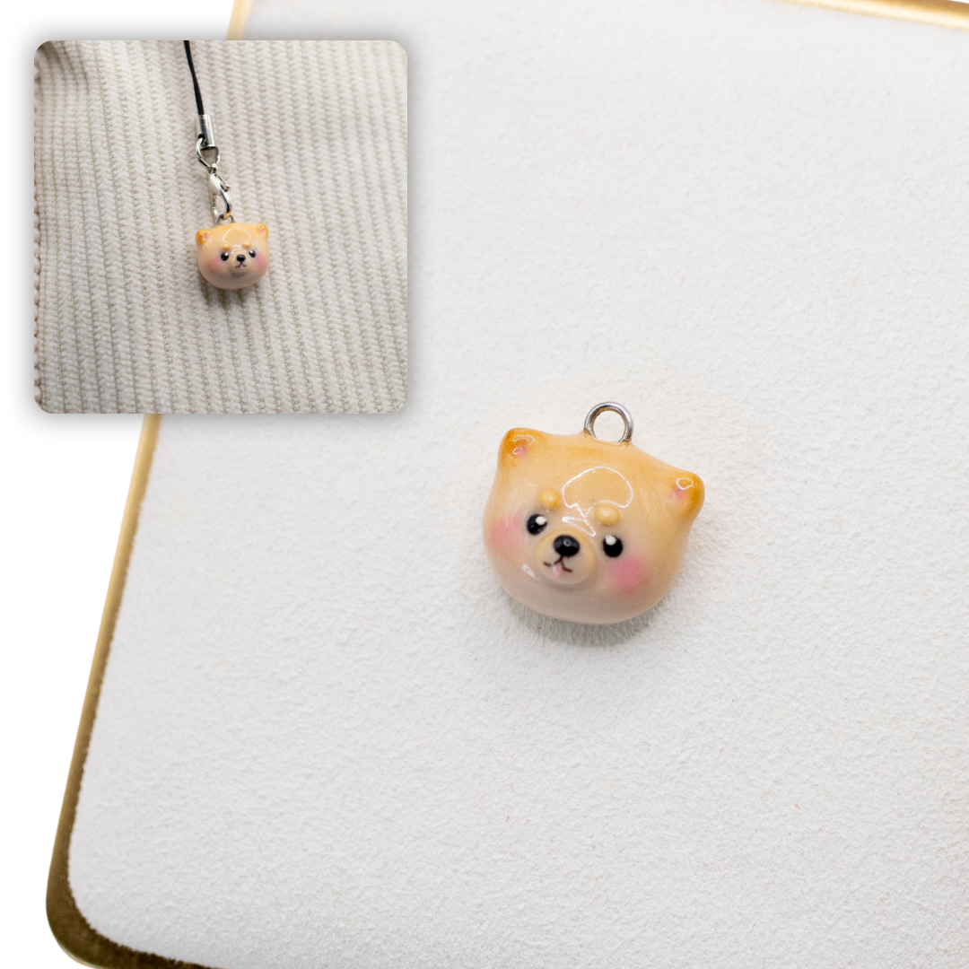 A picture of a pomeranian polymer clay dog charm against a white background, with a 2nd smaller photo of the same dog charm being hung with a phone strap against a textured background.