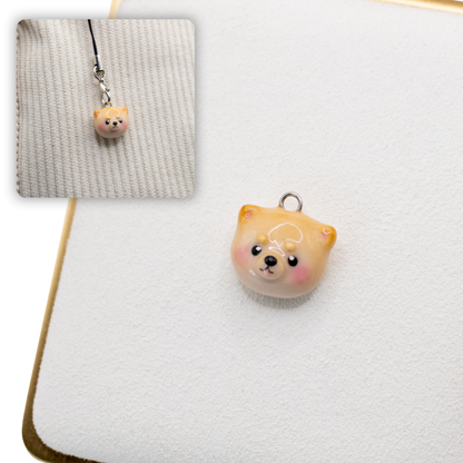 A picture of a pomeranian polymer clay dog charm against a white background, with a 2nd smaller photo of the same dog charm being hung with a phone strap against a textured background.