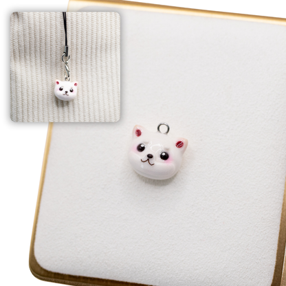A picture of a cream shiba inu polymer clay dog charm on a white display with a gold border. There is a 2nd smaller photo of the same dog charm being hung with a phone strap against a textured background.