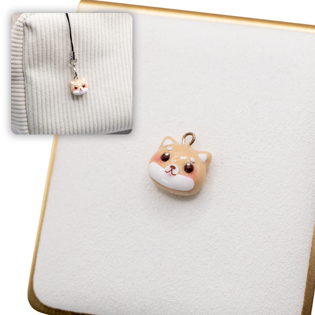 A picture of red shiba inu polymer clay dog charm on a white display with a gold border. There is a 2nd smaller photo of the same dog charm being hung with a phone strap against a textured background.
