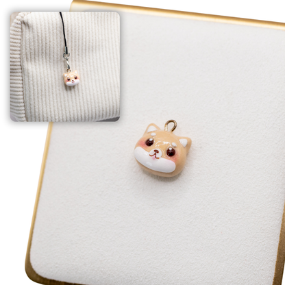 A picture of red shiba inu polymer clay dog charm on a white display with a gold border. There is a 2nd smaller photo of the same dog charm being hung with a phone strap against a textured background.