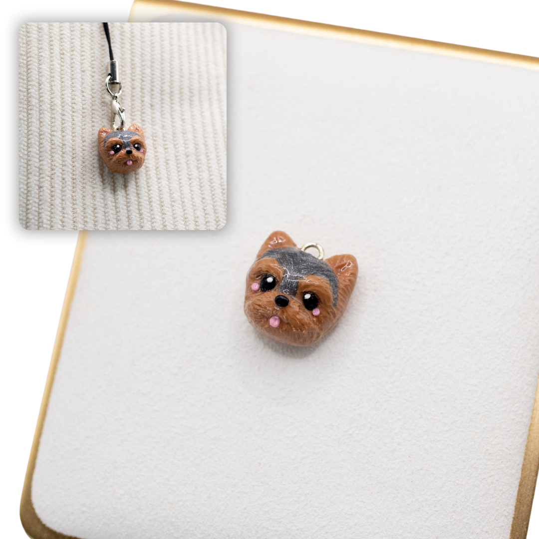 A picture of a yorkshire terrier dog polymer clay dog charm against a white background, with a 2nd smaller photo of the same dog charm being hung with a phone strap against a textured background.